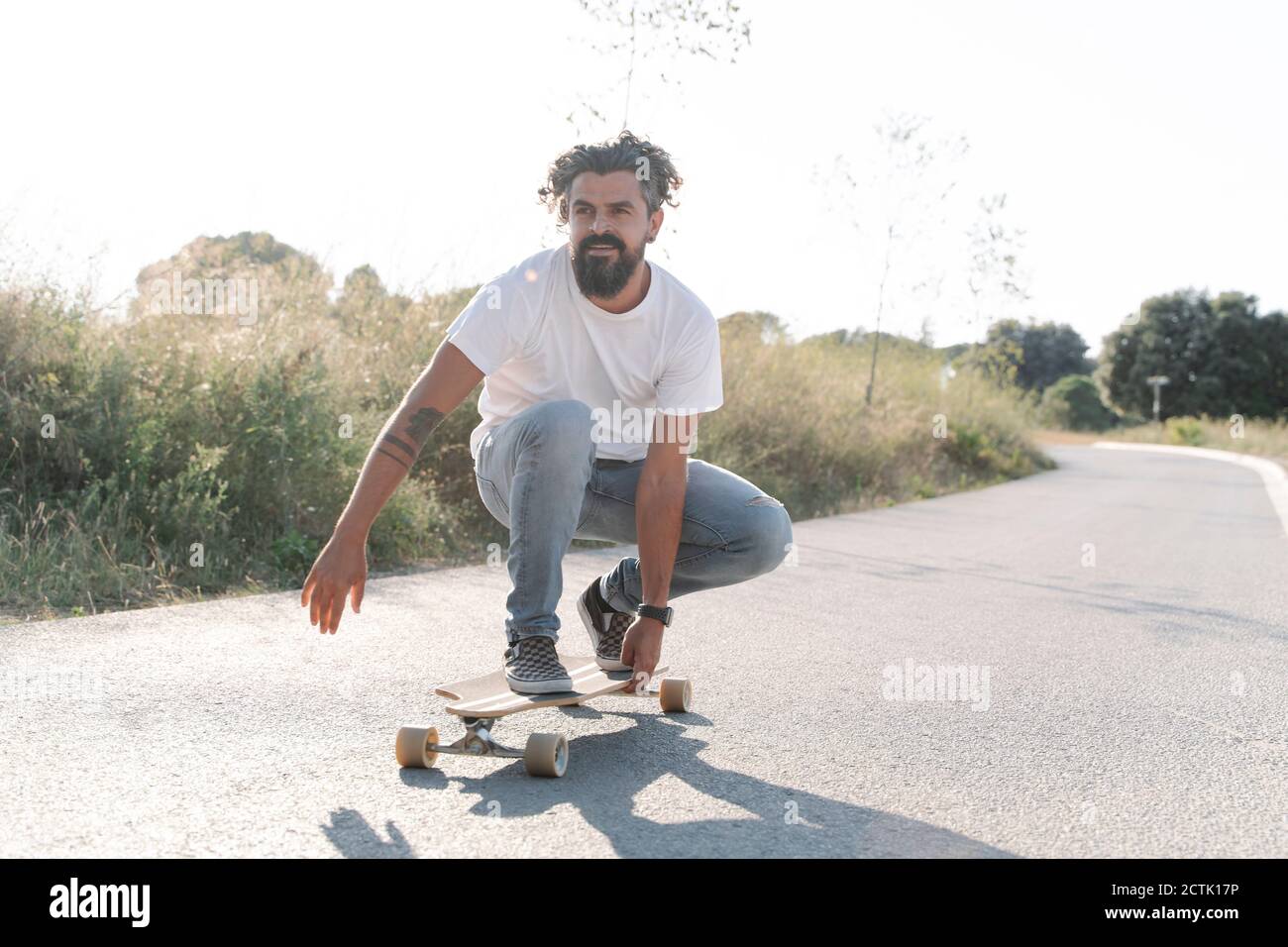 Schöner bärtiger reifer Mann Skateboarding auf der Straße gegen klaren Himmel Stockfoto