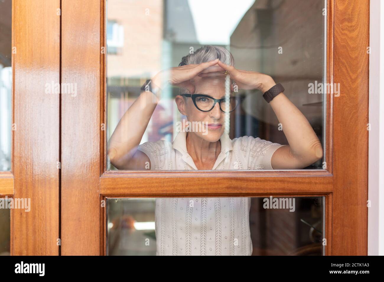 Ältere Frau, die Handbewegung macht, während sie aus dem Fenster schaut Zu Hause Stockfoto