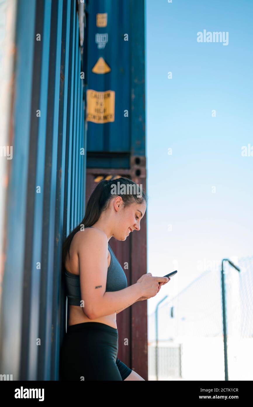 Athletische Frau mit Smartphone im Industriepark Stockfoto