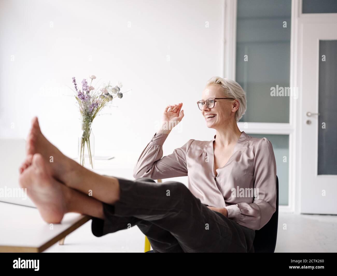 Lächelnde Geschäftsfrau mit Füßen auf dem Schreibtisch, entspannen im Loft-Büro Stockfoto