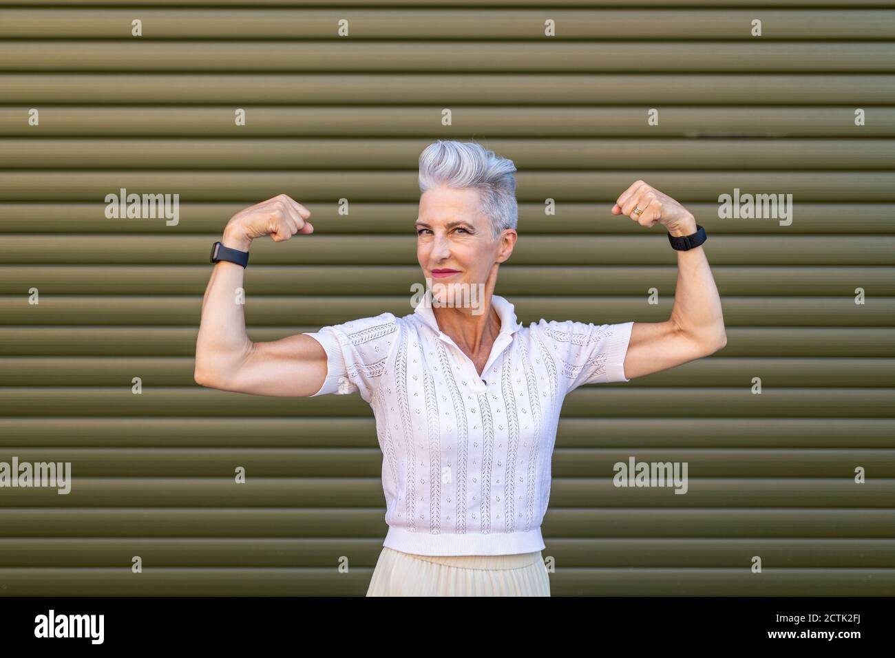 Ältere Frau, die Muskeln beugend, während sie gegen den Verschluss steht Stockfoto