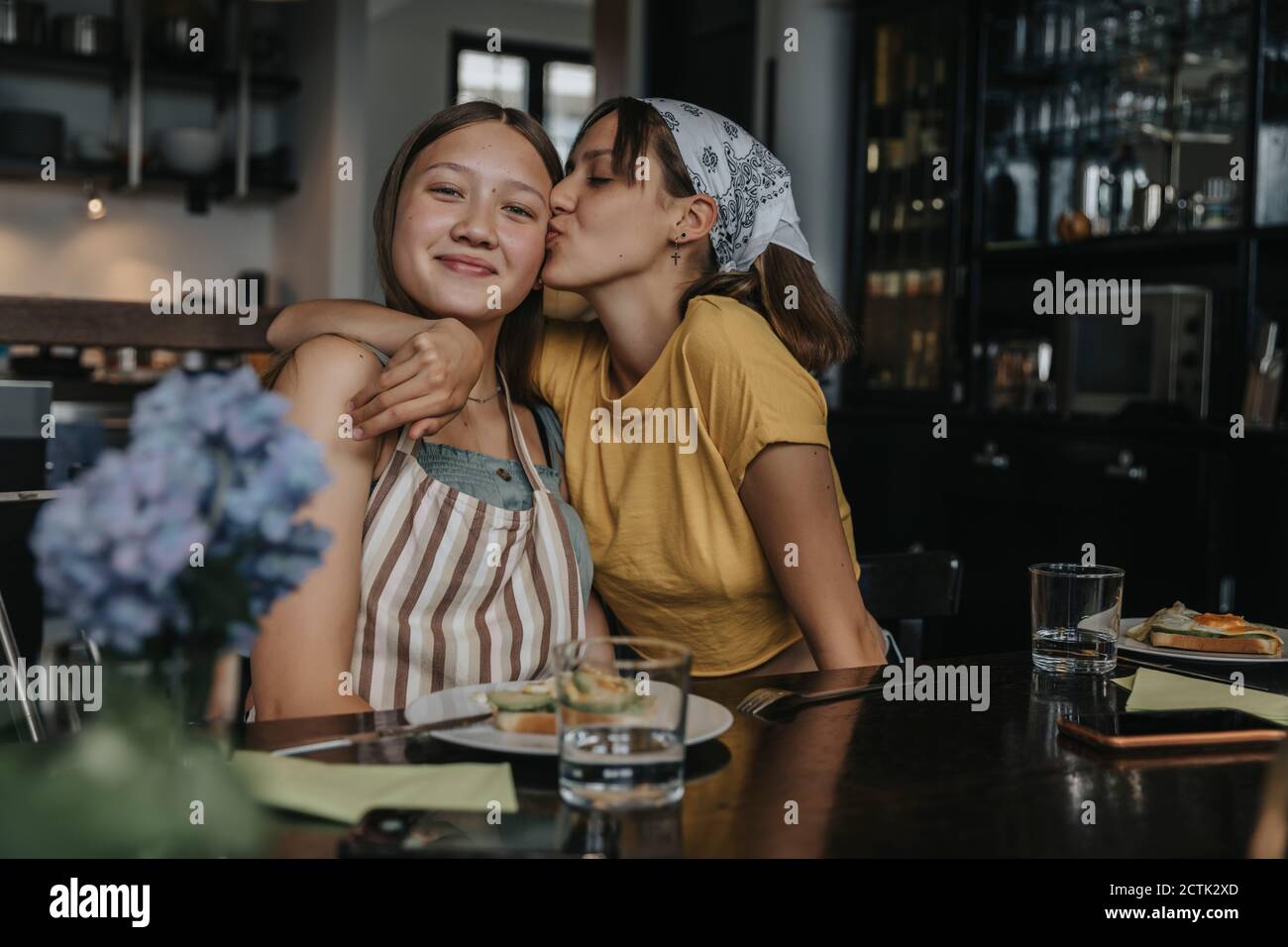 Teenager Freundinnen sitzen am Esstisch, umarmen und küssen Stockfoto