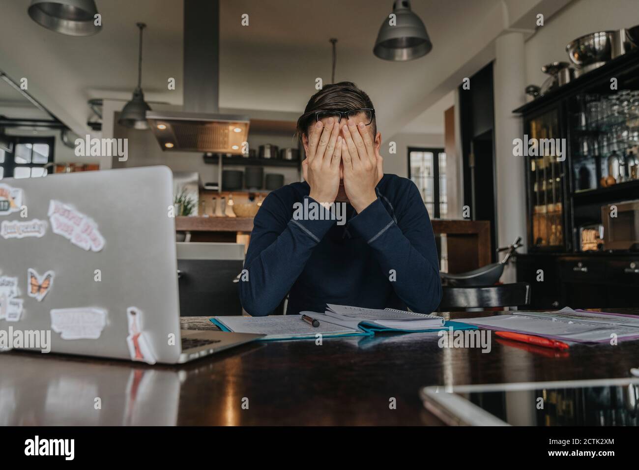 Überstresster junger Mann, der von zu Hause aus studiert und das Gesicht mit den Händen bedeckt Stockfoto