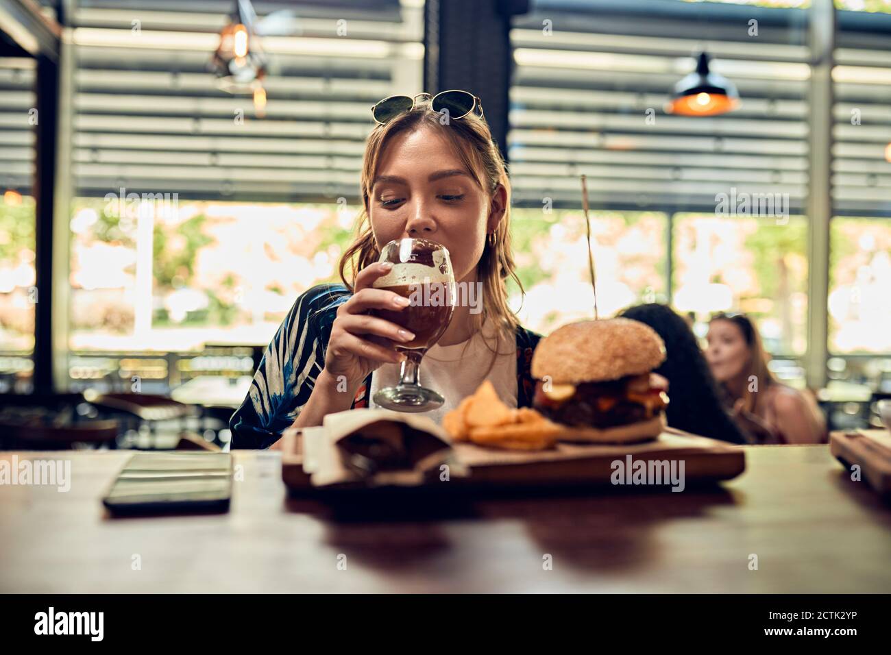 Frau, die ein Bier und einen Burger in einer Kneipe trinkt Stockfoto