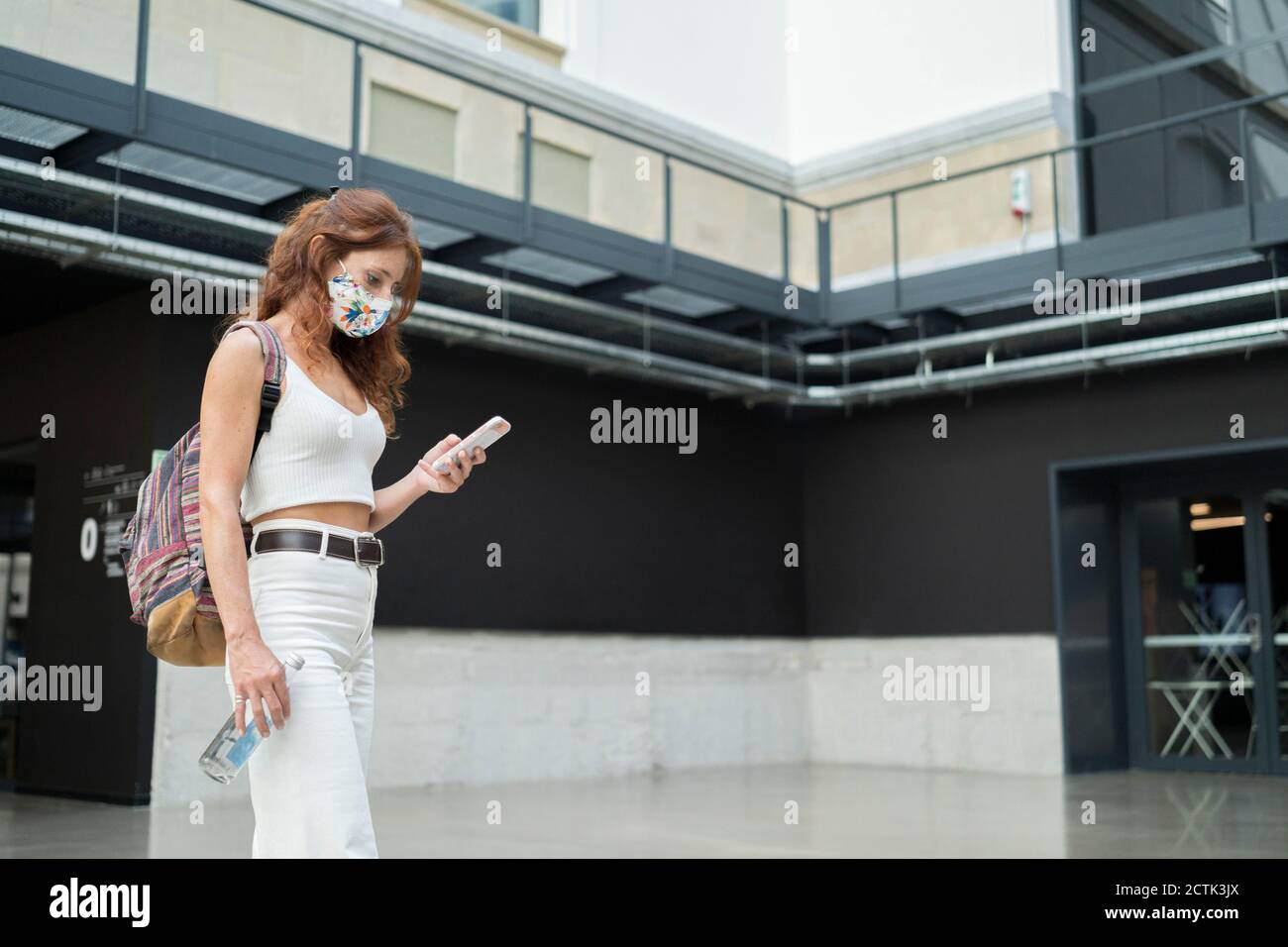 Frau mit Rucksack zu Fuß während der Verwendung von Smartphone während COVID-19 Stockfoto