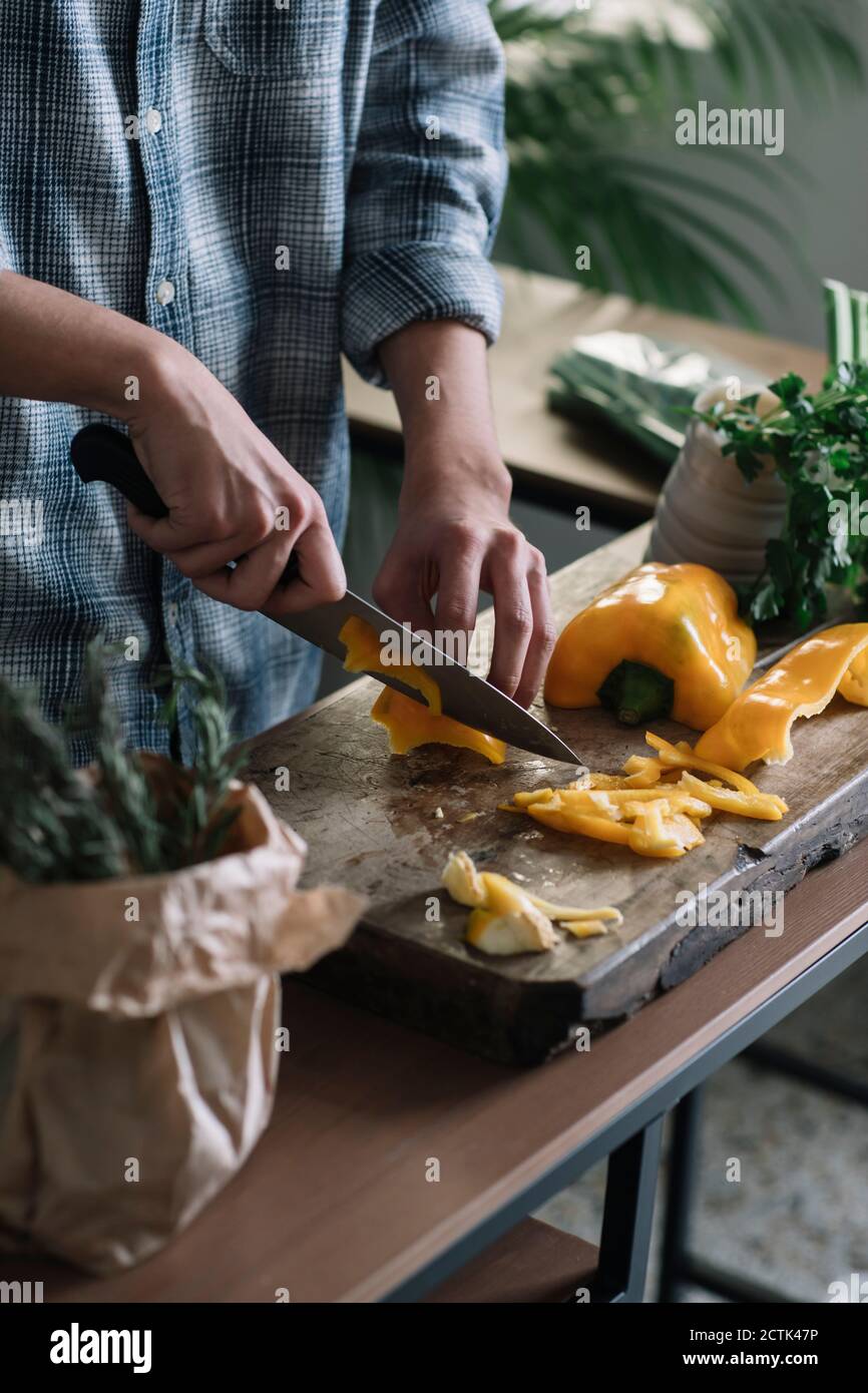 Mittelteil des jungen Mannes, der gelbe Paprika an Bord schneidet In der Küche Stockfoto