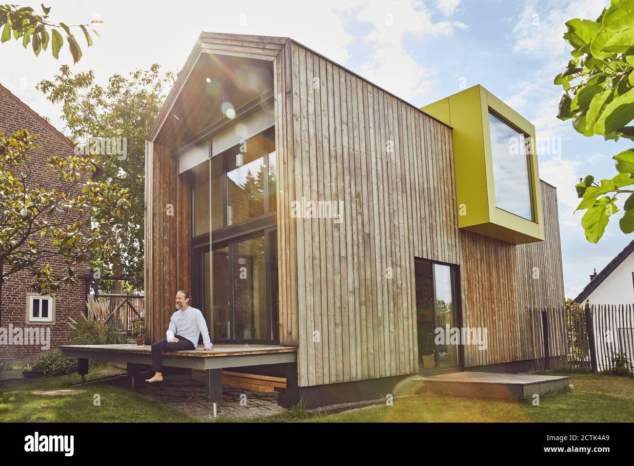 Reifer Mann sitzt außerhalb winzigen Haus im Hof während sonnig Tag Stockfoto