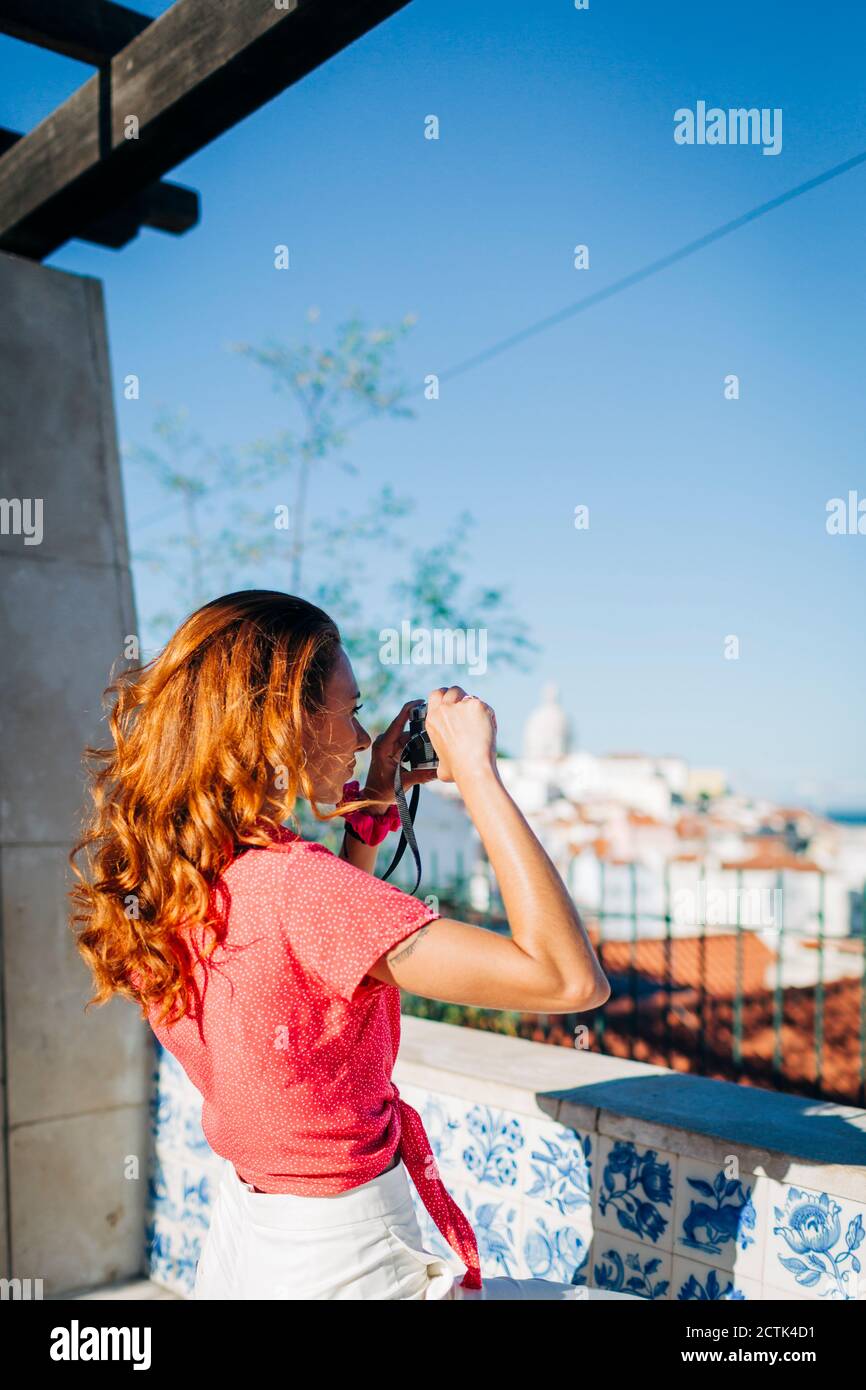 Frau, die den Blick fotografiert, während sie an einer Stützmauer in Alfama, Lissabon, Portugal, steht Stockfoto