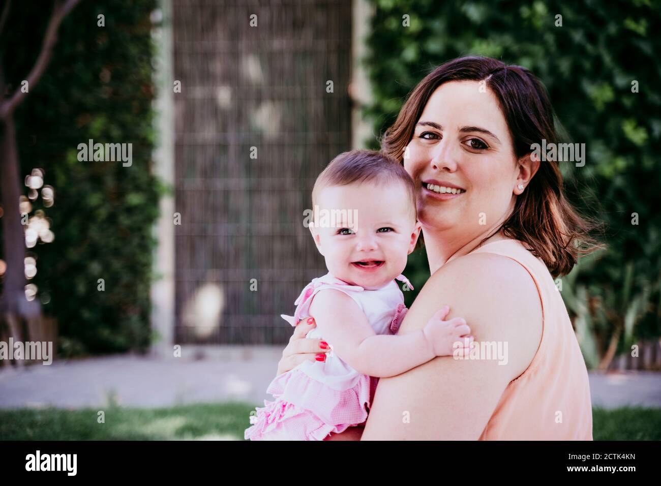 Glückliche Mutter trägt Baby Mädchen im Hinterhof Stockfoto