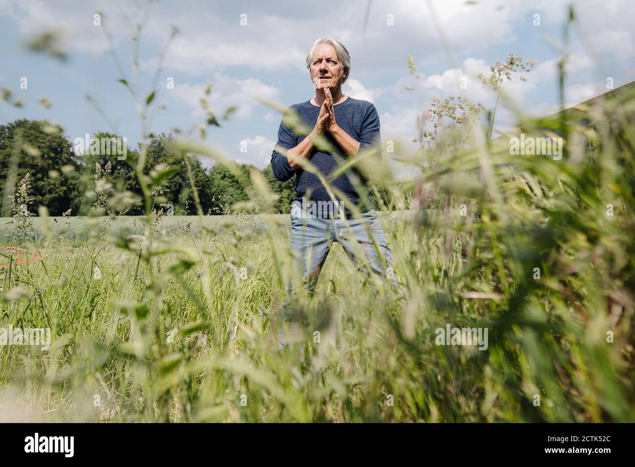 Faltiger Mann mit Händen auf Gras im landwirtschaftlichen Feld umklammerte Stockfoto