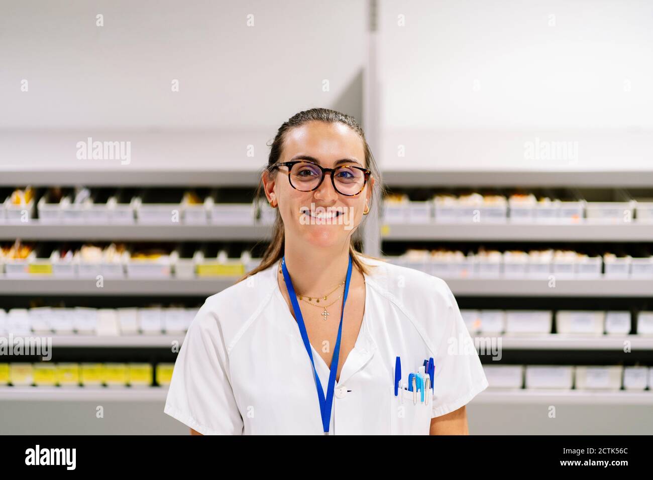 Lächelnde Apothekerin, die im Lagerraum gegen die Medikamentenregale steht Stockfoto
