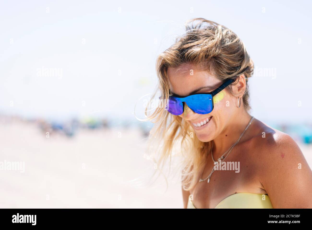 Glückliche junge Frau, die nach unten schaut, während sie gegen den Strand steht Stockfoto