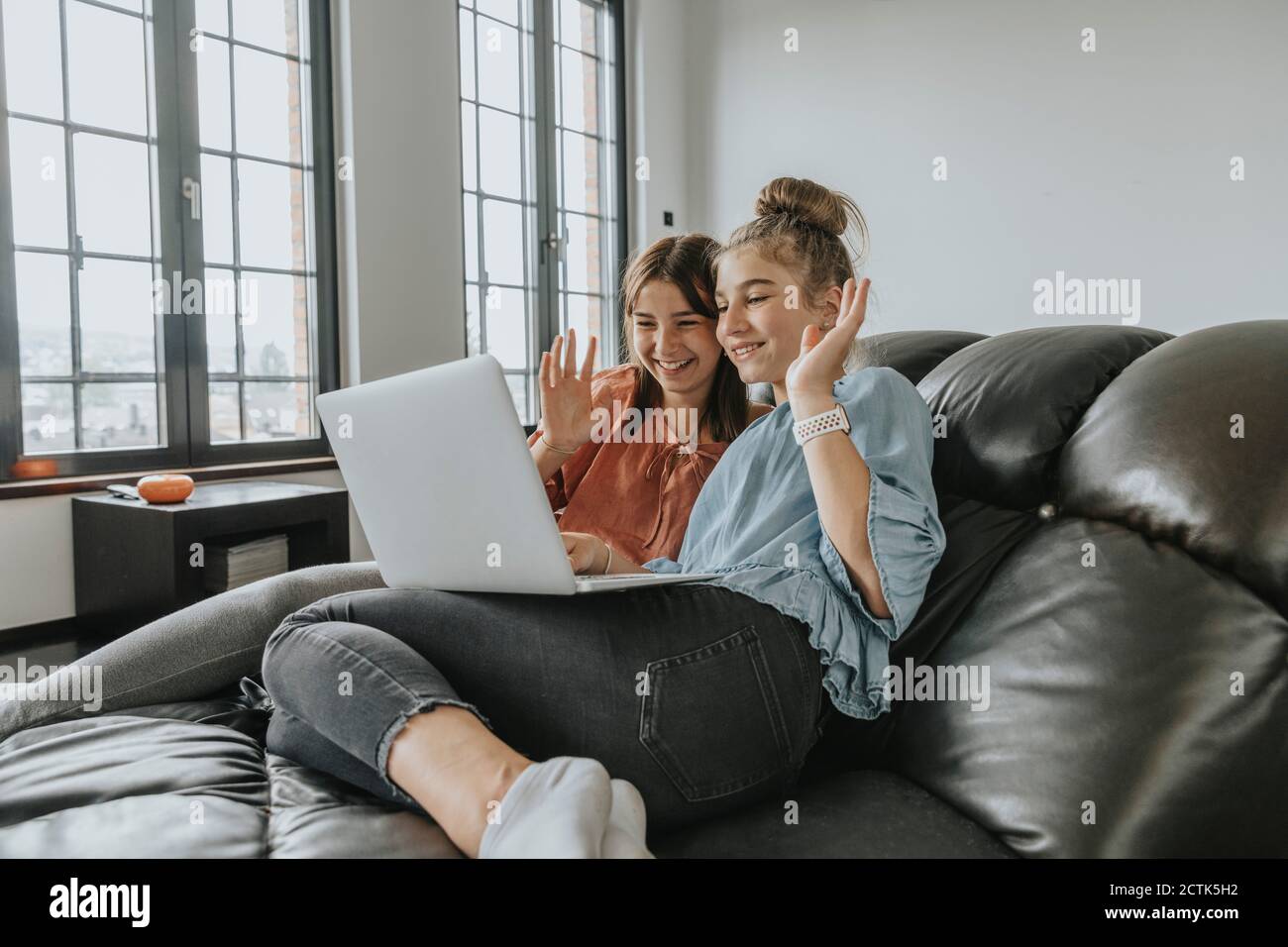 Freunde winken während Videokonferenzen über Laptop auf dem Sofa an Zu Hause Stockfoto