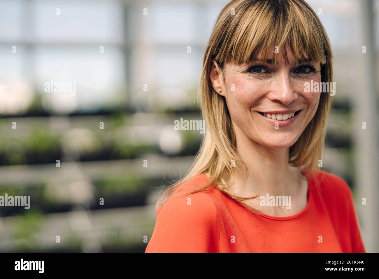 Nahaufnahme einer lächelnden Unternehmerin mit blonden Haaren in der Pflanze Kindergarten Stockfoto