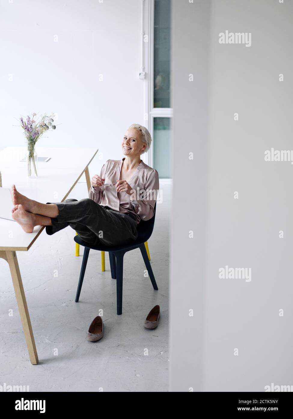 Lächelnde Geschäftsfrau mit den Füßen nach oben auf einem Stuhl im Loft entspannen Büro Stockfoto