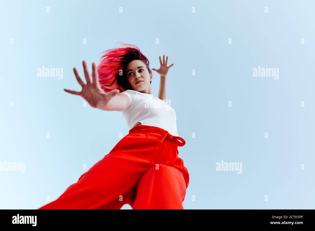 Junge Frau mit gefärbten roten Haaren tun Stop-Geste, während Stehen gegen klaren Himmel Stockfoto