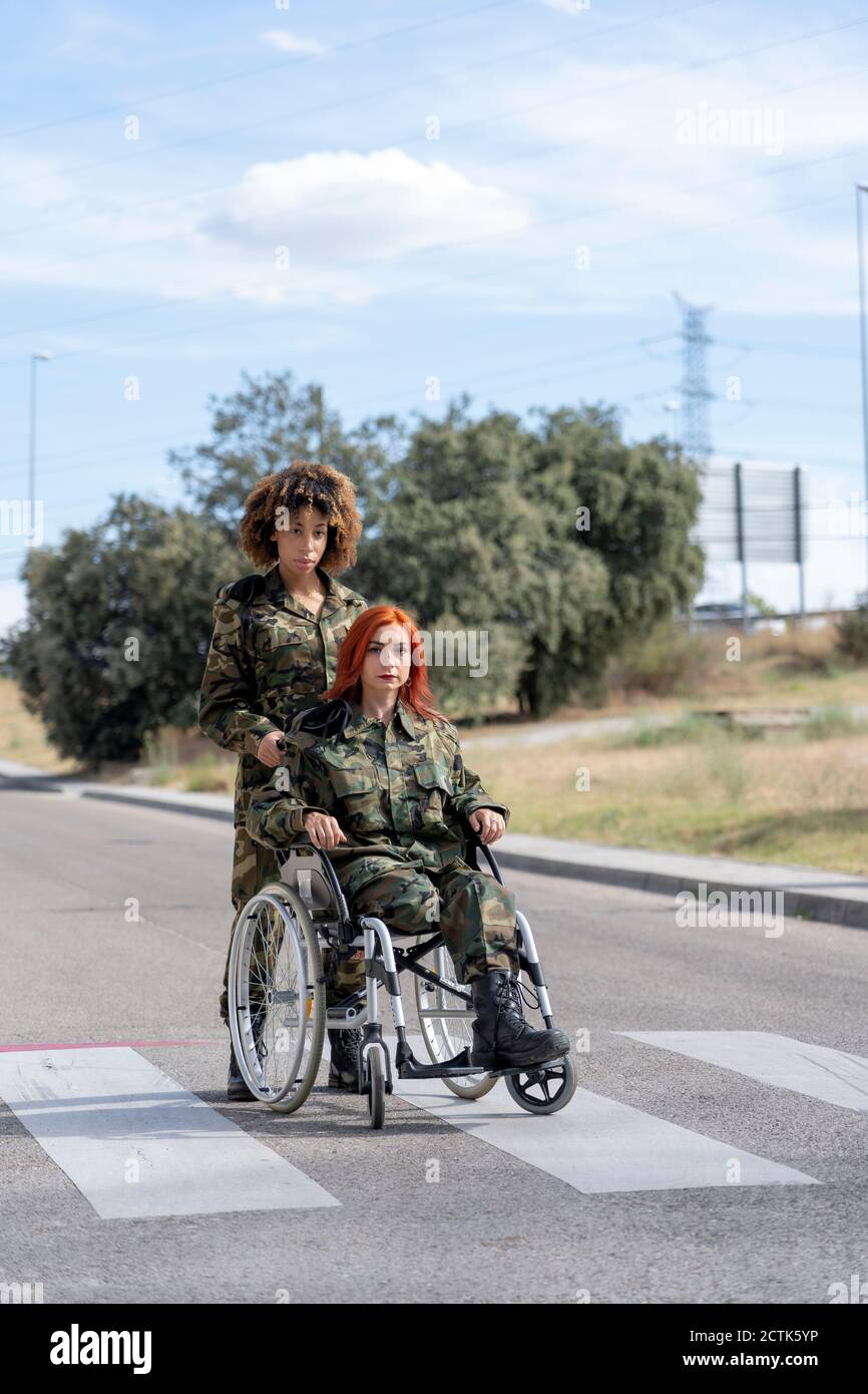 Armeesoldat hilft behinderten Militäroffizier auf Rollstuhl im Stehen Auf der Straße Stockfoto