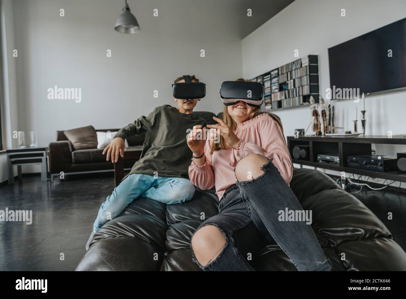 Begeisterte Freunde, die durch Virtual Reality-Simulatoren schauen, während sie sich entspannen Couch zu Hause Stockfoto