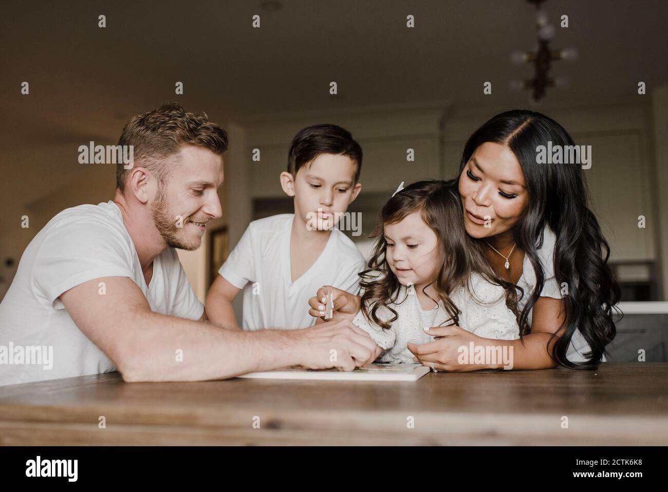 Lächelnde Eltern lösen Puzzle mit Kindern auf dem Tisch bei Zu Hause Stockfoto