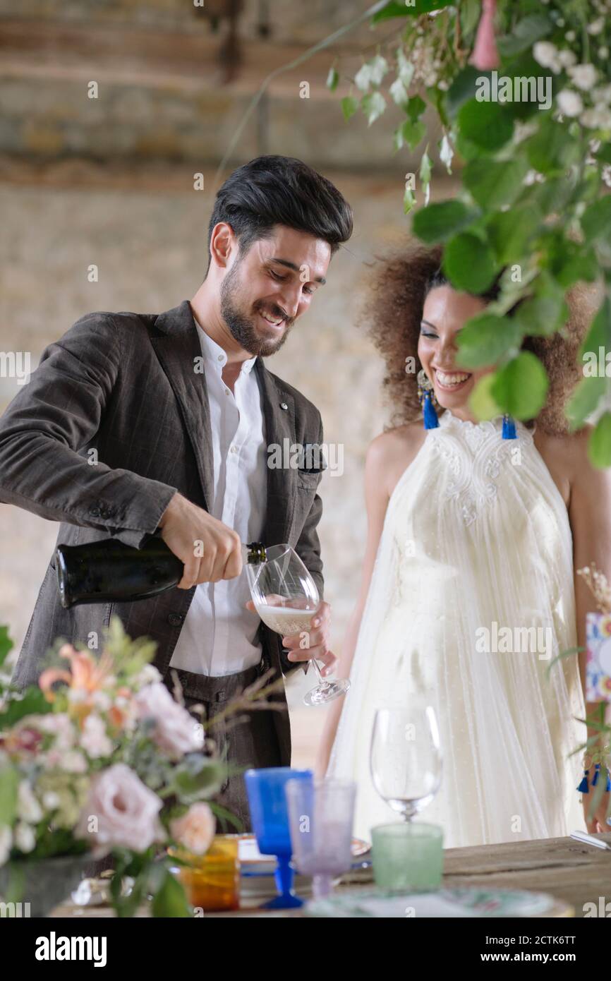 Lächelnder Bräutigam gießt Champagner in Flöte, während er am Tisch steht Stockfoto