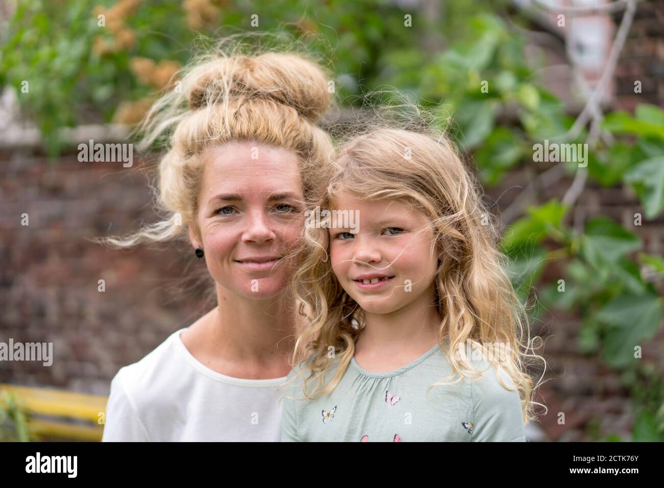 Lächelnde blonde Frau mit Tochter im Hinterhof Stockfoto