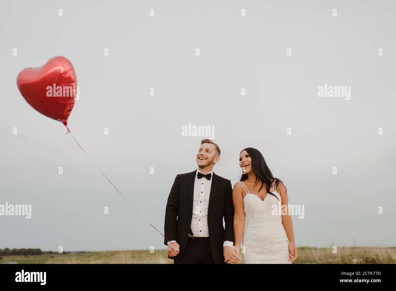 Glückliche Braut und Bräutigam mit Herz-Form Ballon gegen Himmel Stockfoto