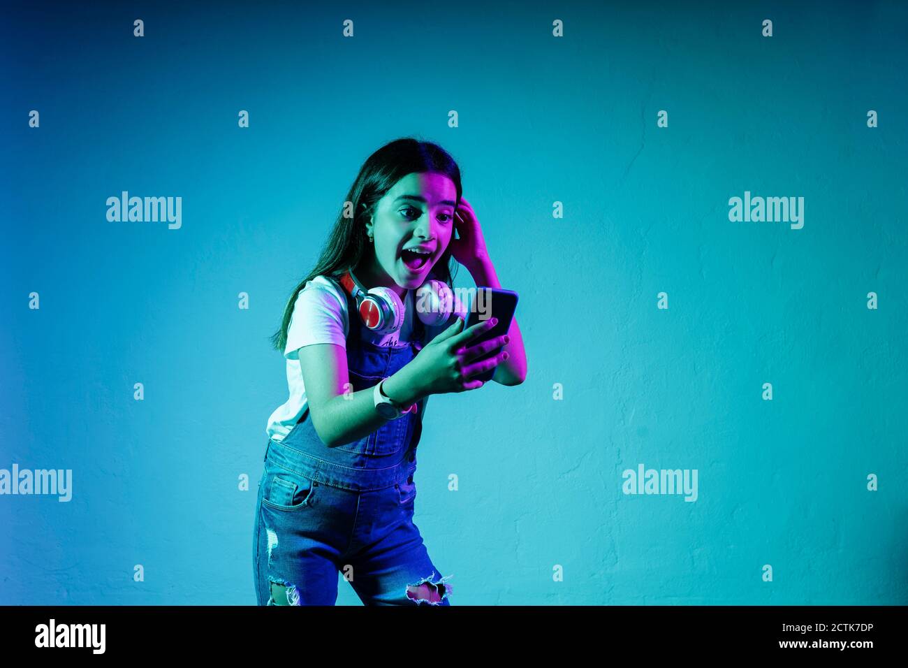 Aufgeregt Mädchen Blick auf Smartphone beim Stehen gegen blau Hintergrund Stockfoto