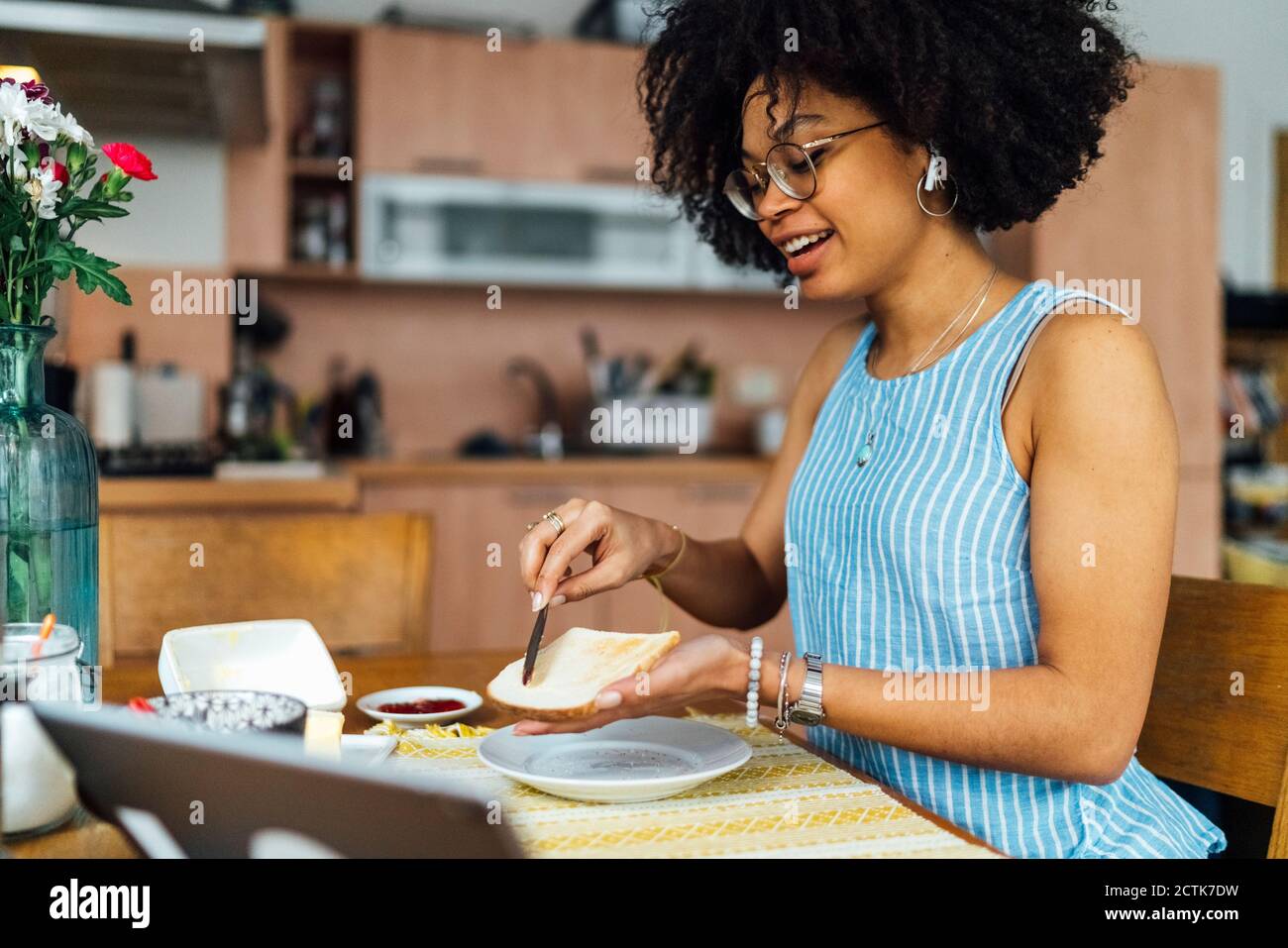 Junge Frau mit lockigen Haaren, die Brot auf dem Tisch schlaff Zu Hause Stockfoto