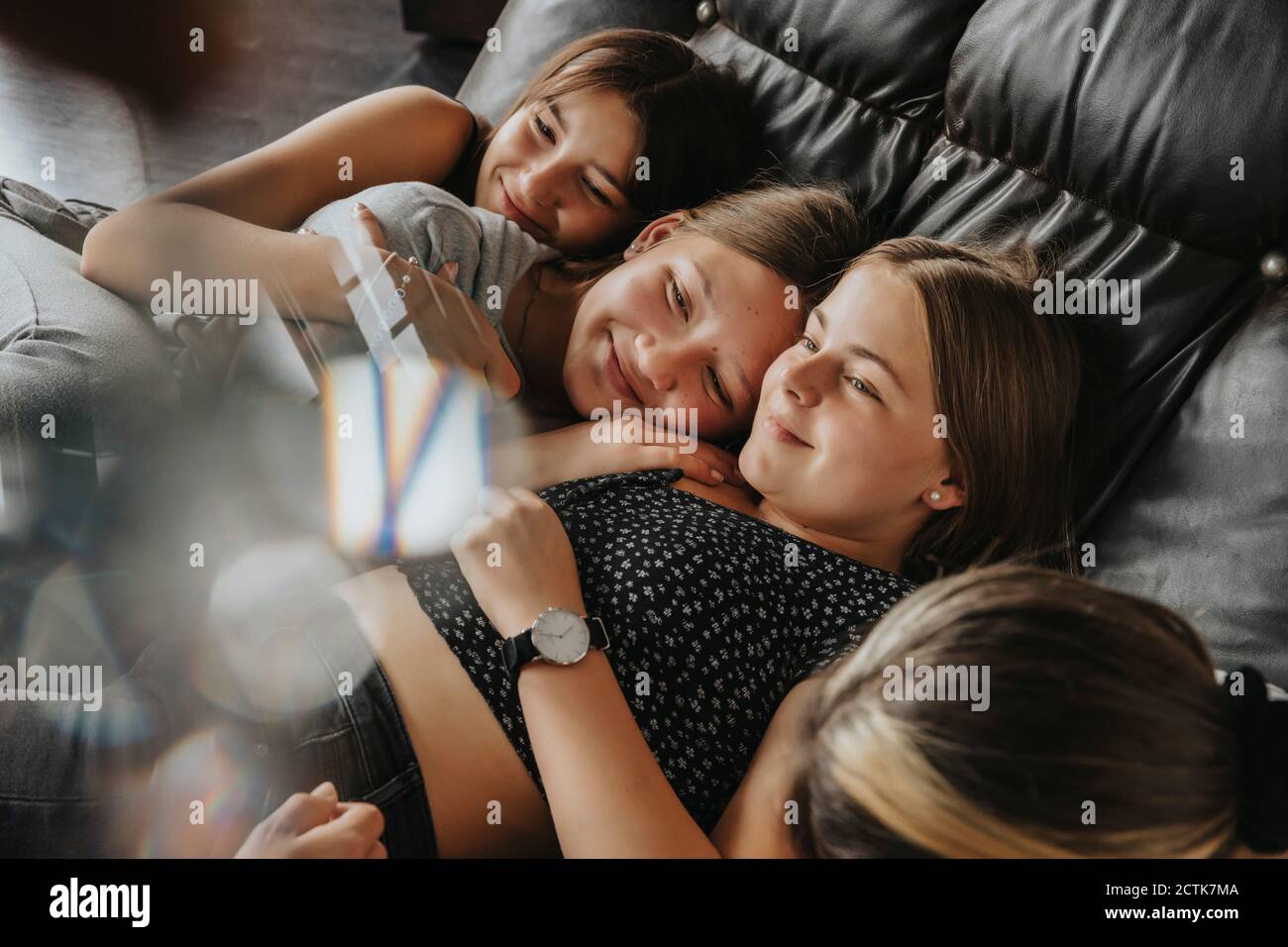 Lächelnde Freunde kuscheln, während sie zu Hause auf dem Schlafsofa liegen Stockfoto