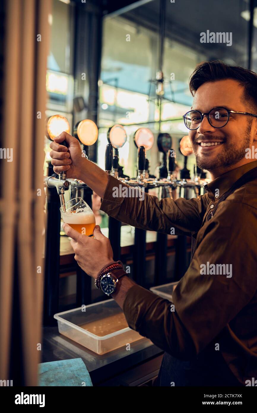 Porträt eines lächelnden Barkeepers, der in einer Kneipe Bier zapft Stockfoto