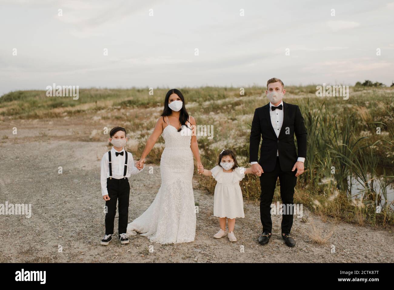 Eltern und Kinder im Hochzeitskleid tragen Gesichtsmaske, während Während des COVID-19 im Feld stehen Stockfoto