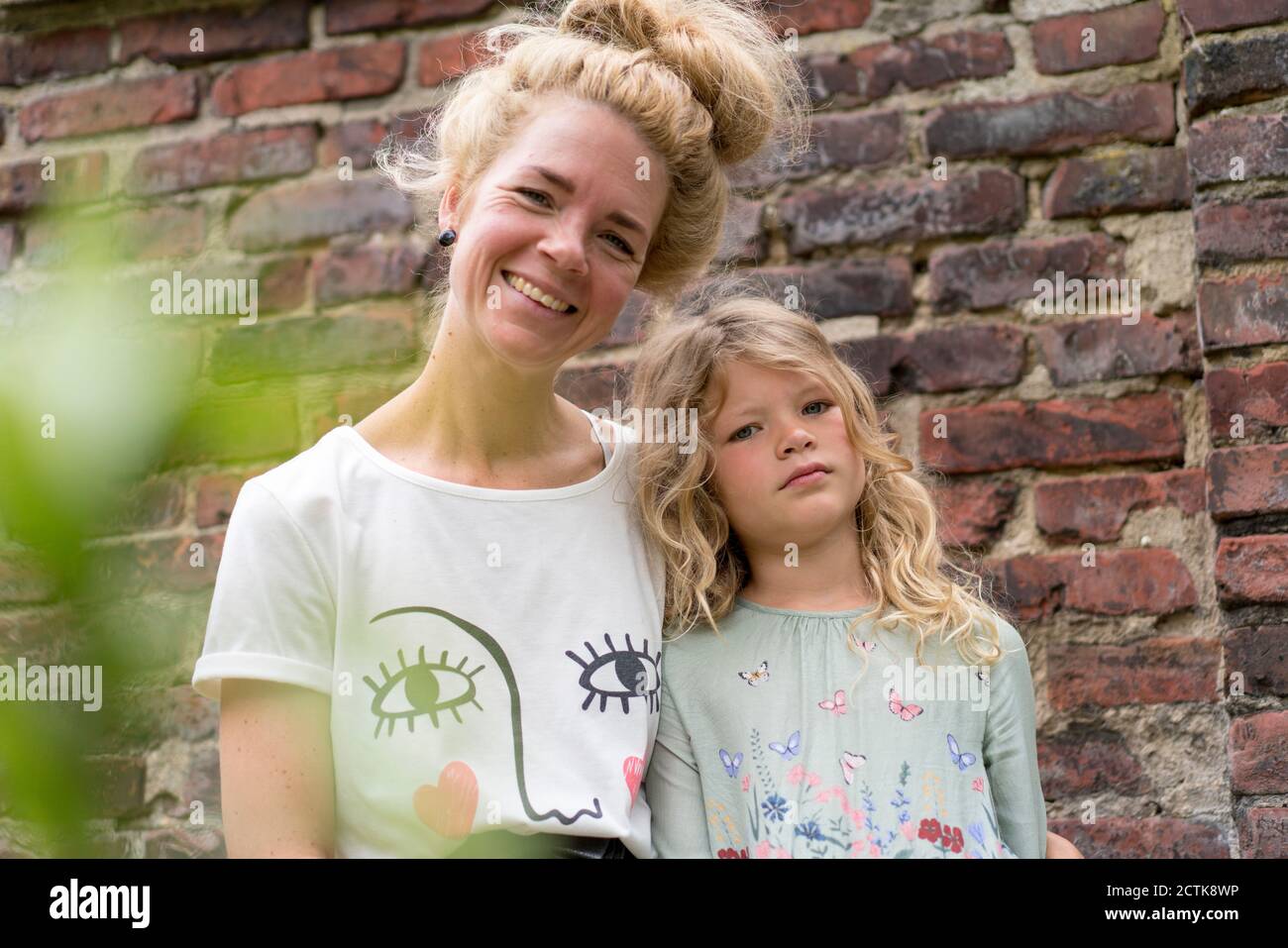 Lächelnde blonde Frau mit Tochter gegen Backsteinmauer auf der Rückseite Hof Stockfoto