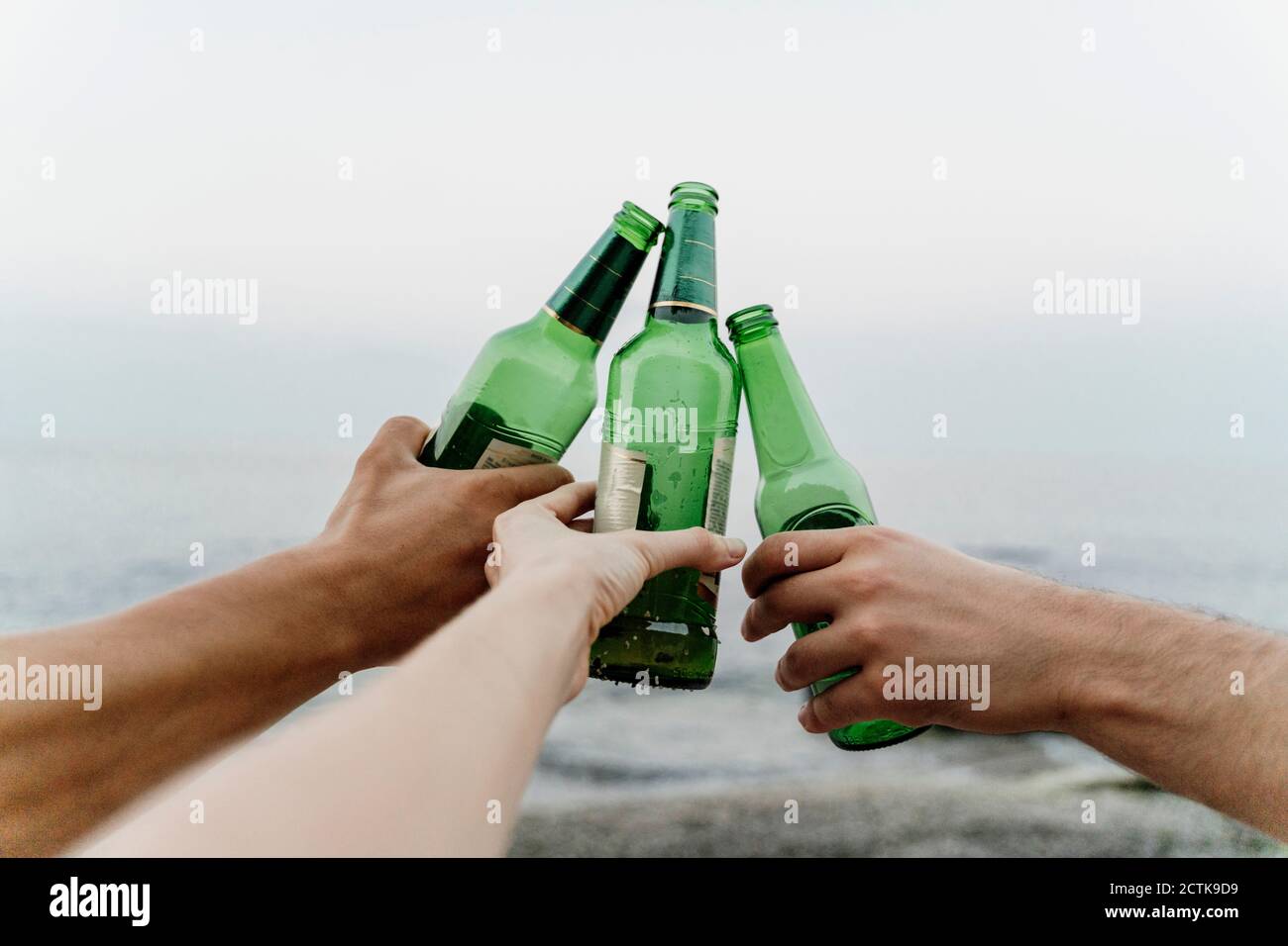 Hände von drei Freunden, die feierlichen Toast mit Bierflaschen machen Stockfoto