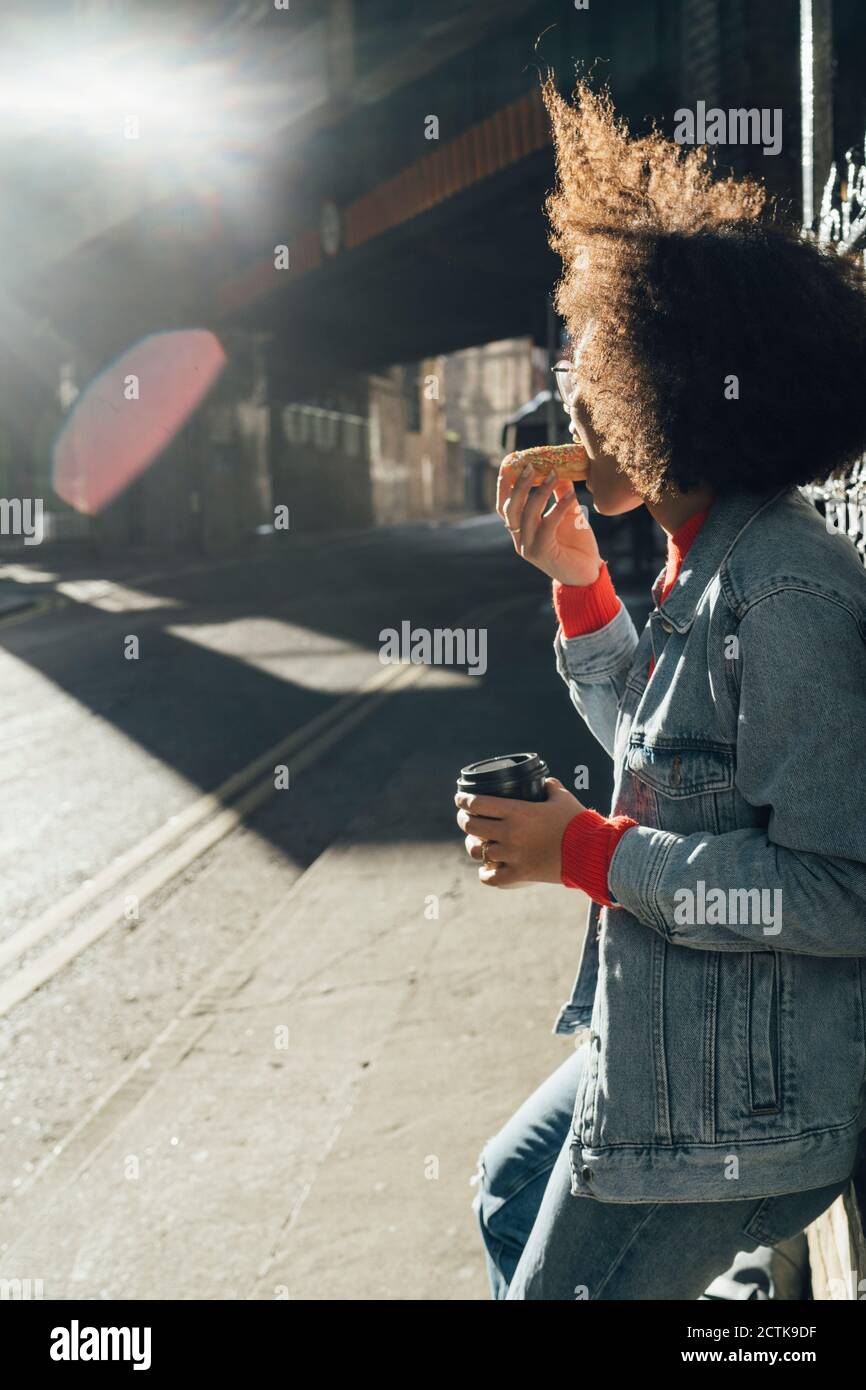 Afro junge Frau essen Donut, während auf der Straße stehen während Sonniger Tag Stockfoto