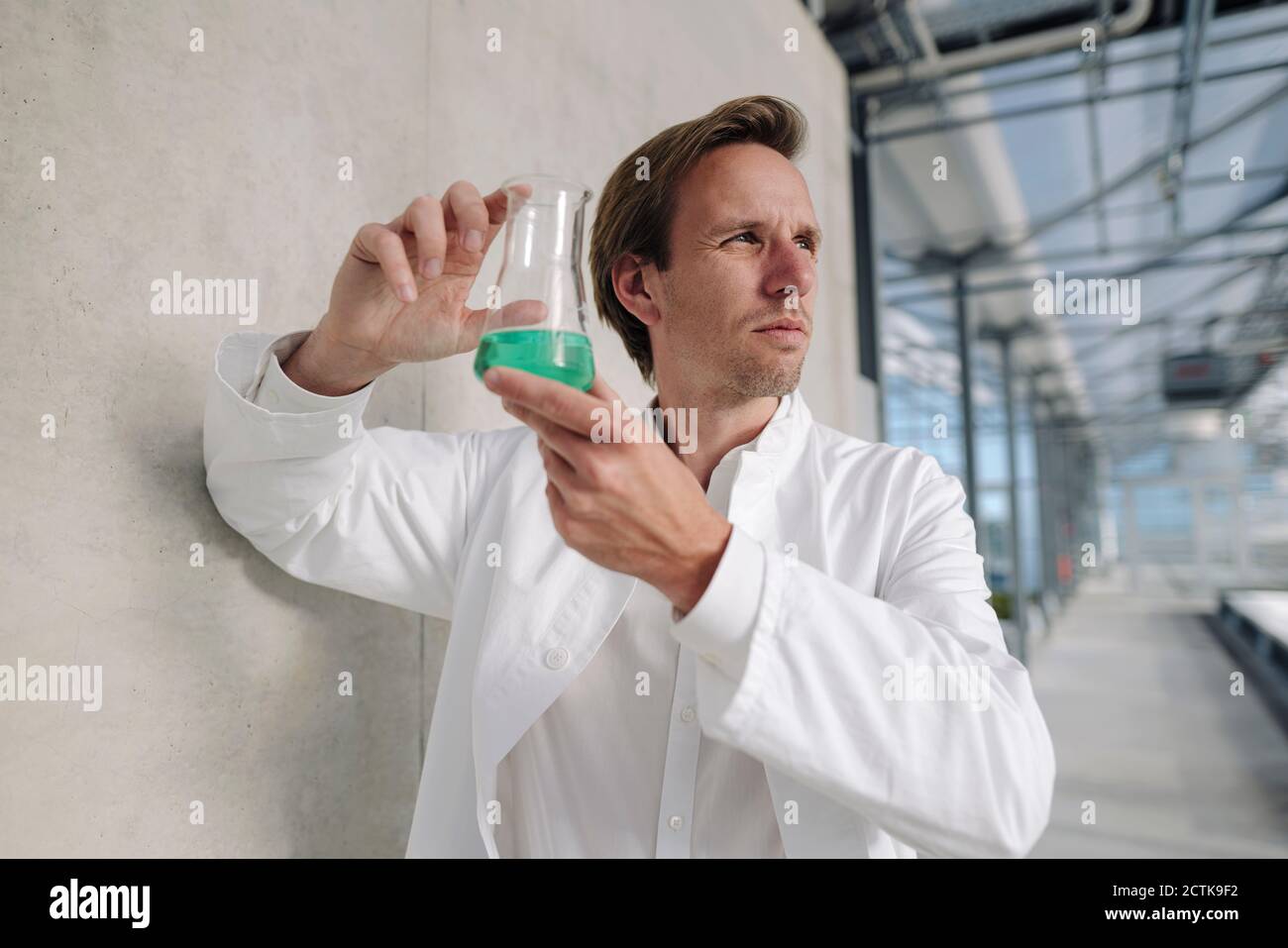 Wissenschaftler hält Becher mit Flüssigkeit an einer Wand Stockfoto