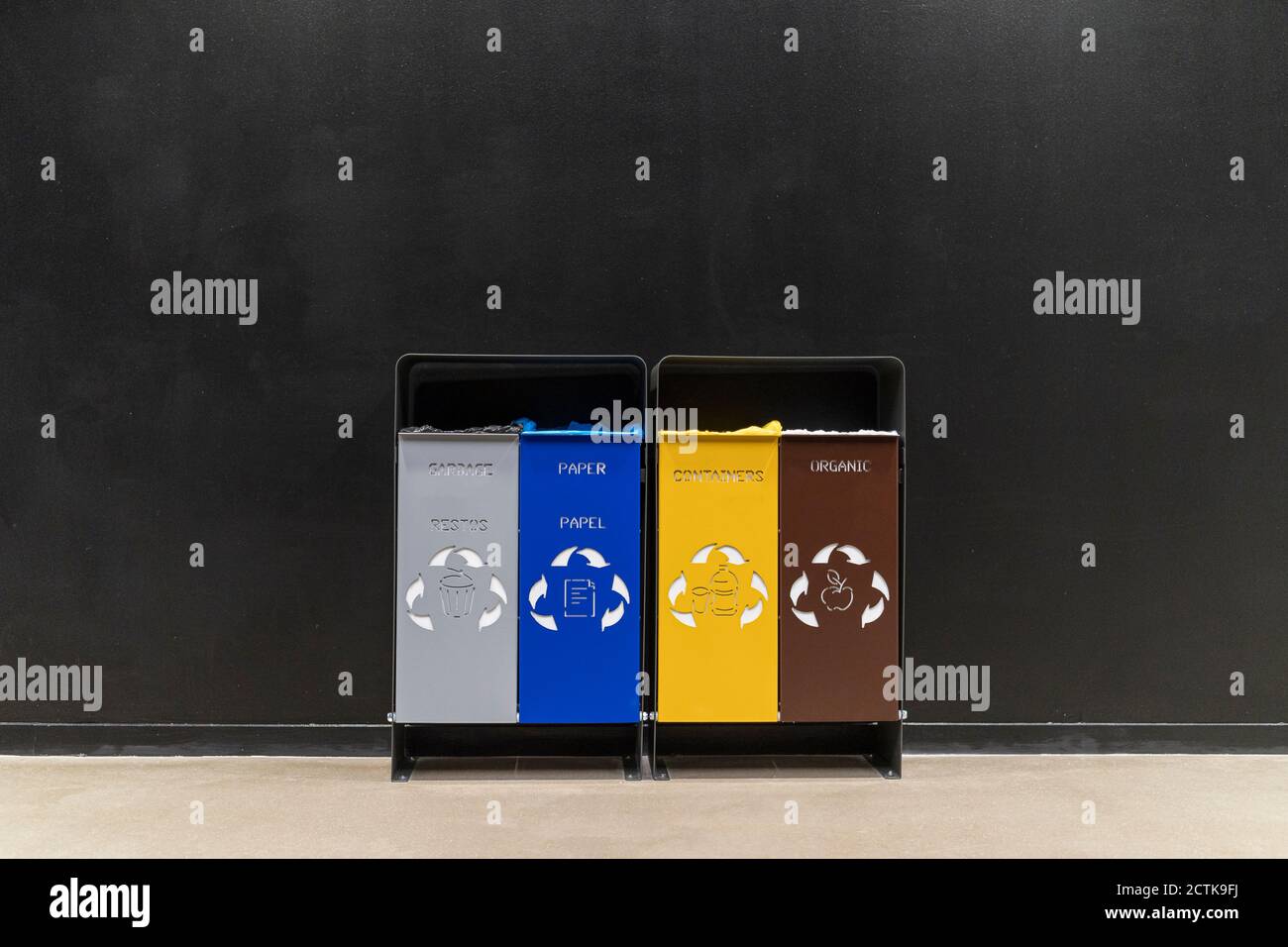 Bunte Mülltonnen mit Recycling-Symbolen gegen schwarze Wand in Korridor Stockfoto