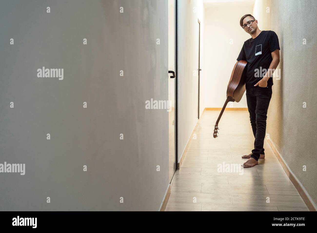 Selbstbewusster Musiker, der Gitarre hält, während er im Korridor steht Stockfoto
