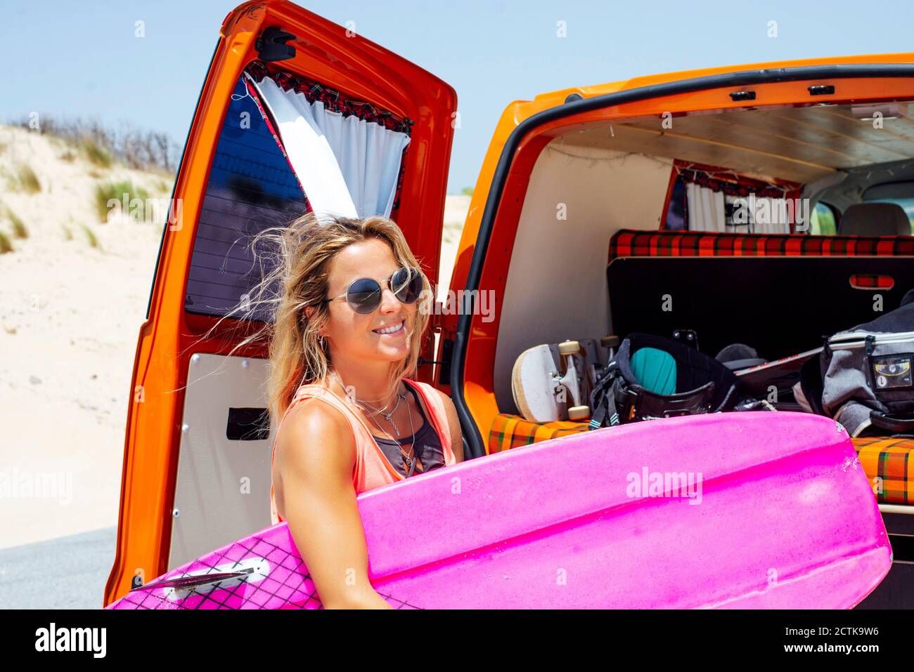 Weibliche Reisende mit Surfbrett, während sie gegen den Kofferraum stehen Stockfoto