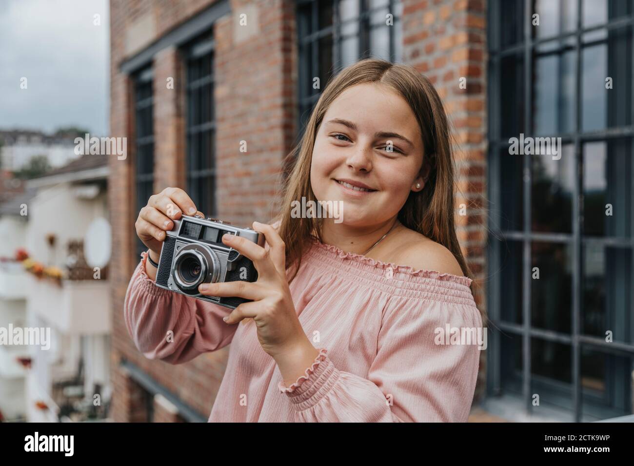 Nahaufnahme eines lächelnden Mädchens mit einer alten Kamera, die vor dem Haus steht Stockfoto