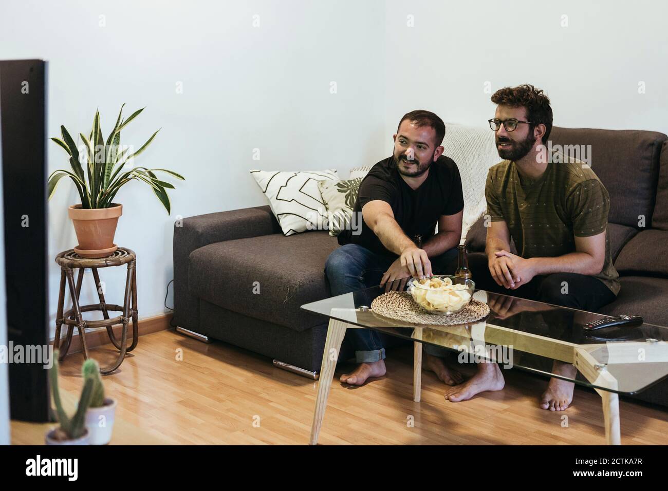 Männliche Freunde schauen Sport im Fernsehen, während sie auf dem Sofa sitzen Im Wohnzimmer Stockfoto