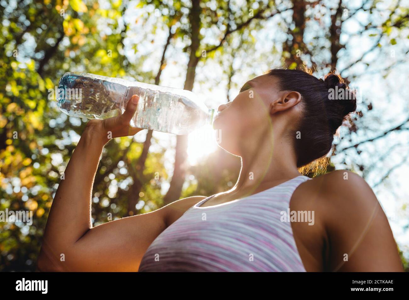 Frau, die Wasser aus einer Plastikflasche in der Sonne trinkt Stockfoto