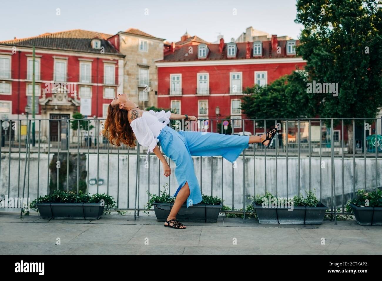 Junge Frau, die sich rückwärts beugte, während sie ein Bein durch Geländer in der Stadt Alfama, Lissabon, Portugal, stand Stockfoto