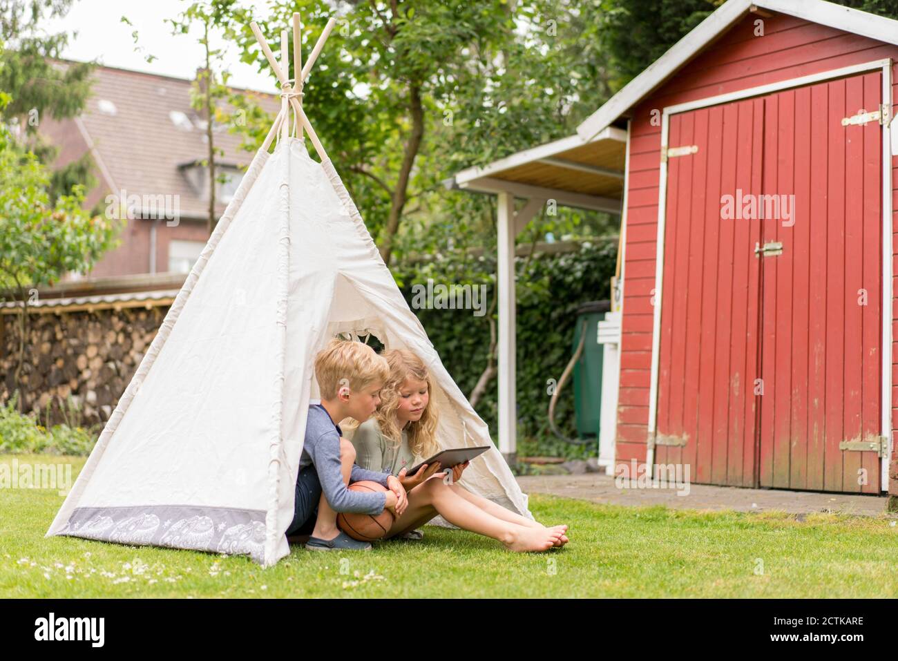 Blonde Kinder mit digitalen Tablet im Zelt auf Gras sitzen Am Wochenende im Hinterhof Stockfoto