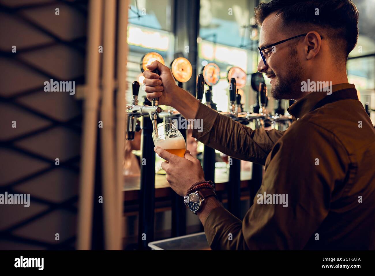 Lächelnder Barkeeper, der in einem Pub Bier zapft Stockfoto