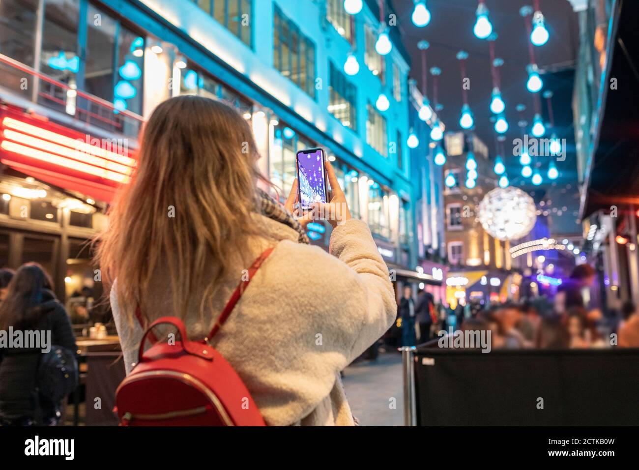 Junge Frau fotografiert beleuchtete Weihnachtslichter hängen in der Stadt an Nacht Stockfoto