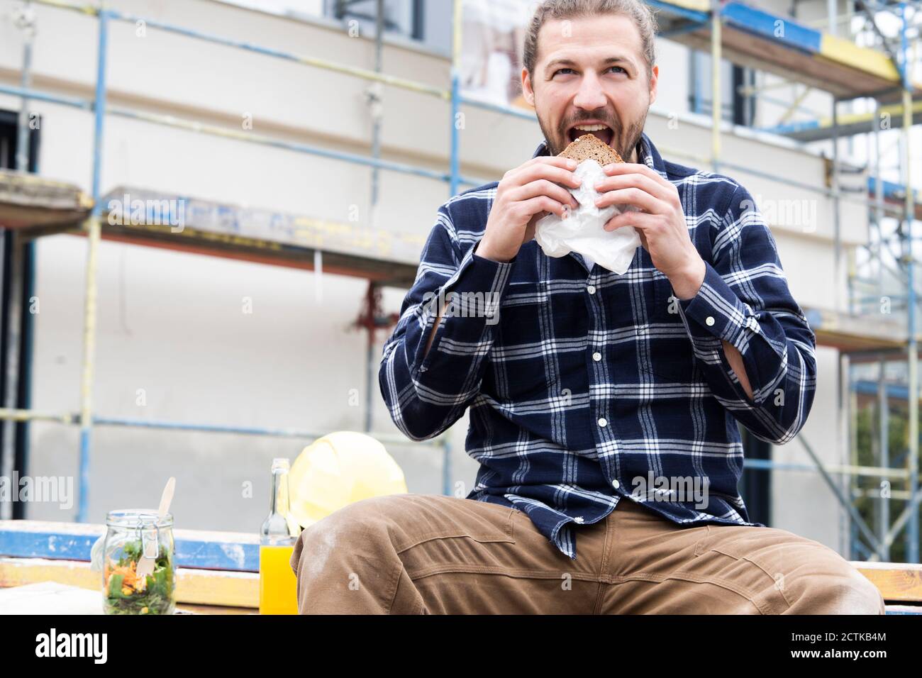 Bauarbeiter essen Brot, während sie gegen Gebäude an der Baustelle sitzen Standort Stockfoto