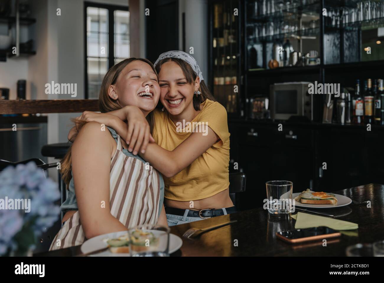 Teenager Freundinnen sitzen am Esstisch, umarmen und lachen Stockfoto