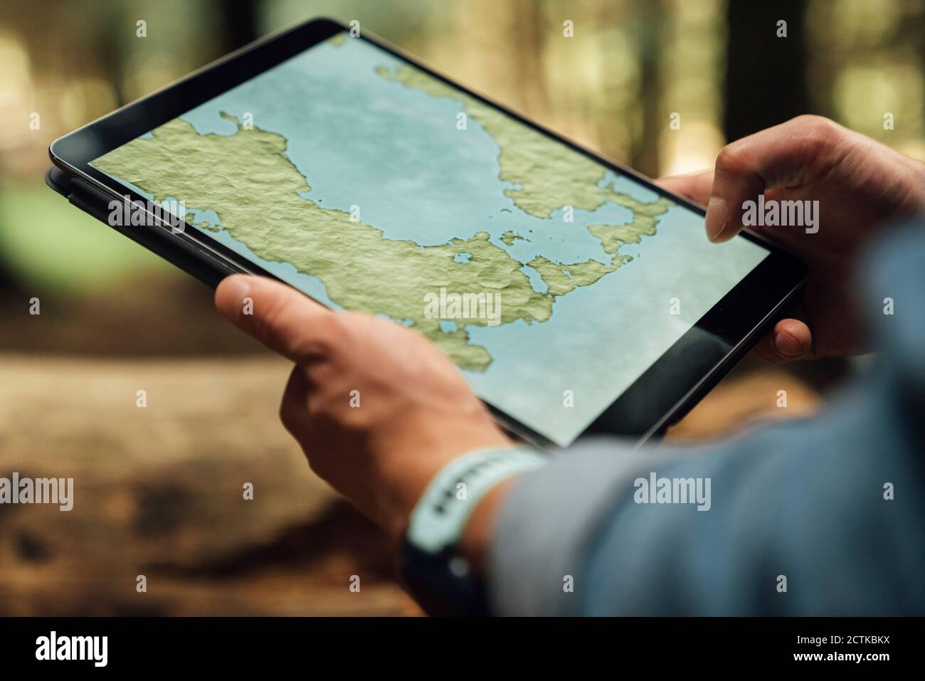 Nahaufnahme der Hände eines Mannes mit mittlerem Erwachsenenalter, die Karte über Digital analysieren Tablet im Wald Stockfoto