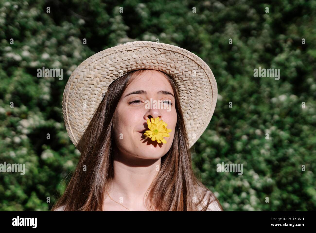 Junge Frau trägt Hut, während die gelbe Blume im Mund Im Frühling im Park Stockfoto