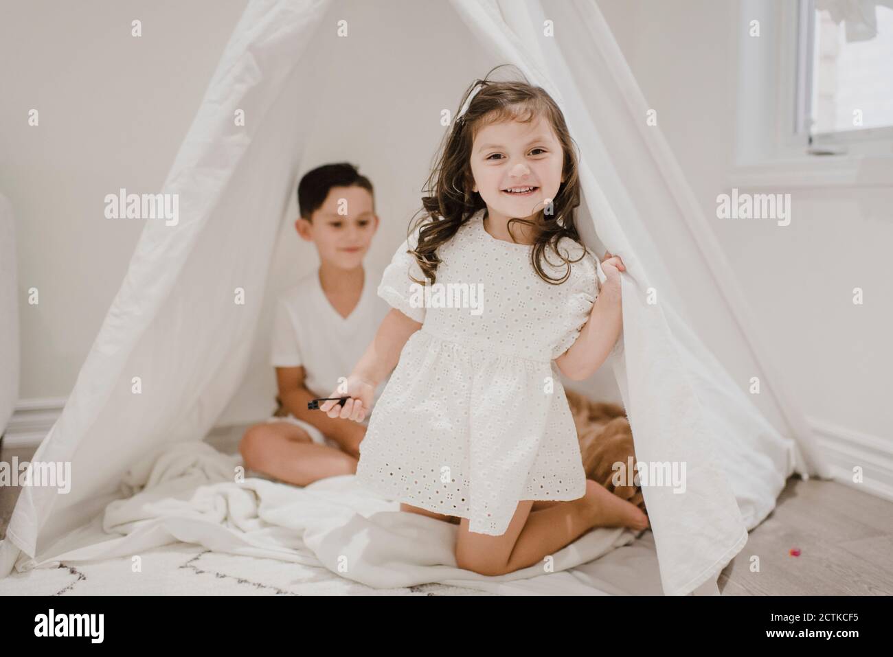Lächelnde Schwester mit Bruder kniet im Zelt zu Hause Stockfoto